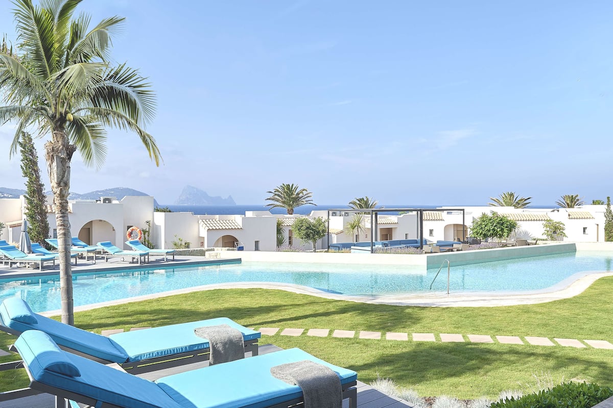 Zona de piscina con sillones de descanso, palmeras y una vista despejada de montañas al fondo.