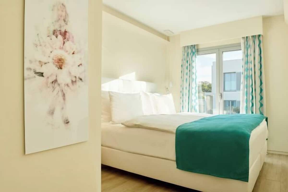 Un dormitorio con cama, una ventana con cortinas y una obra de arte colgada en la pared.