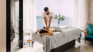 Une séance de massage dans une pièce dotée d’une grande fenêtre donnant sur un plan d’eau, avec un lit et une petite table sur laquelle se trouve un plateau.