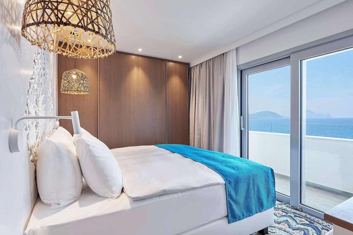 Habitación de hotel moderna con cama, un amplio ventanal con vista al mar y una lámpara en el techo.