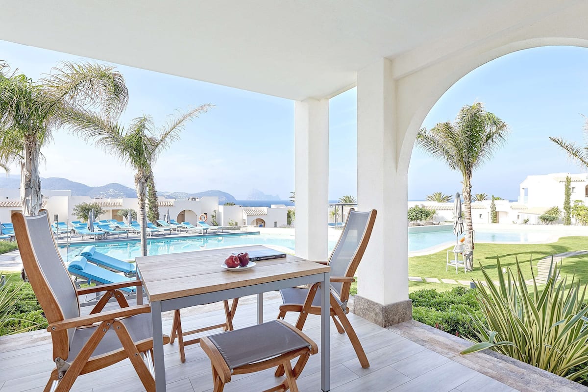 Un espacio al aire libre techado con piscina, sillas de descanso y una mesa con un libro y fruta.
