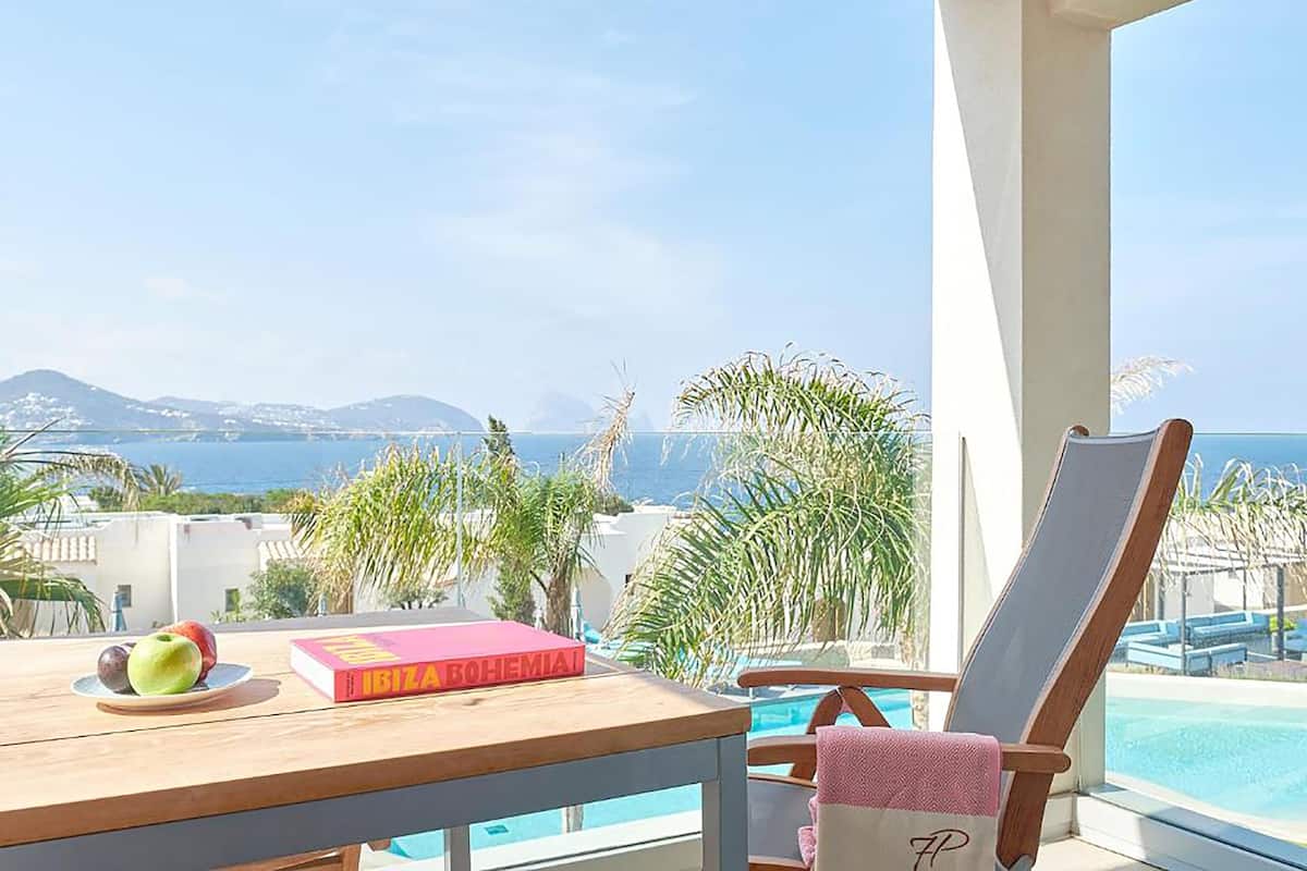 Un balcón con vistas al mar, una piscina y una mesa con un libro y fruta.