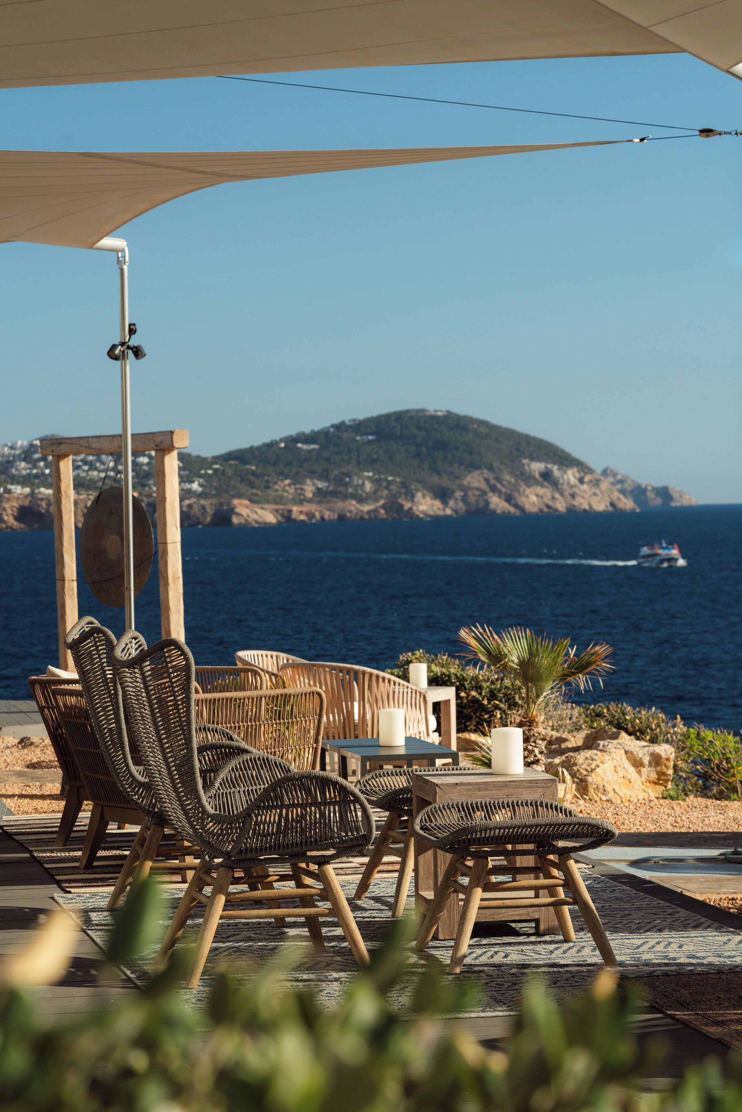 Outdoor seating with wicker chairs and a table, overlooking a body of water and a mountainous landscape.