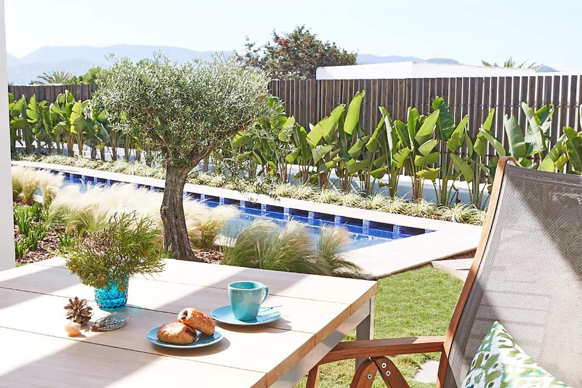 Un patio con piscina, una mesa con una taza y pasteles, y vistas a montañas.