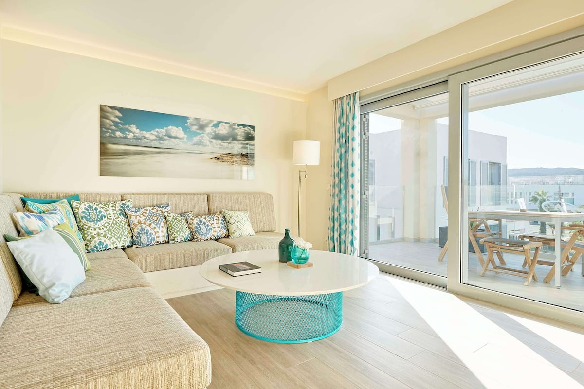 Un salón moderno con sofá, una mesita redonda y un ventanal con vistas a la ciudad.