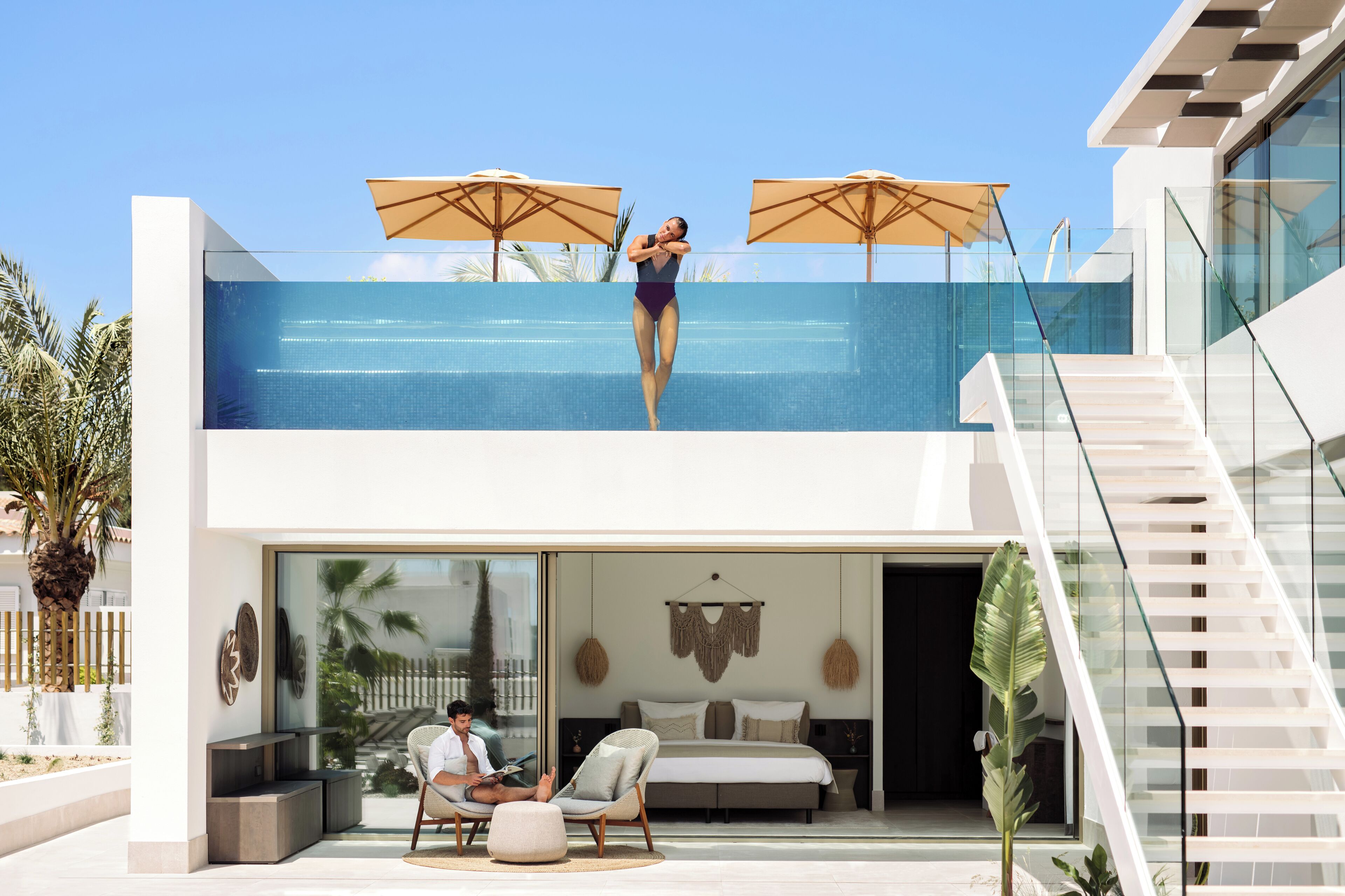 Un hotel moderno con piscina en la azotea, un dormitorio con cama grande y zona de comedor con mesas al aire libre.
