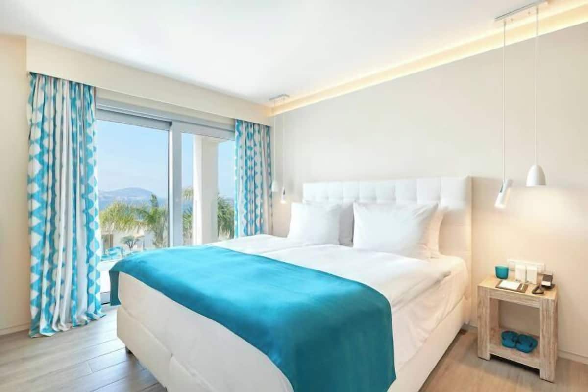 Una habitación de hotel con cama, mesita de noche, vistas por la ventana y una lámpara en el techo.