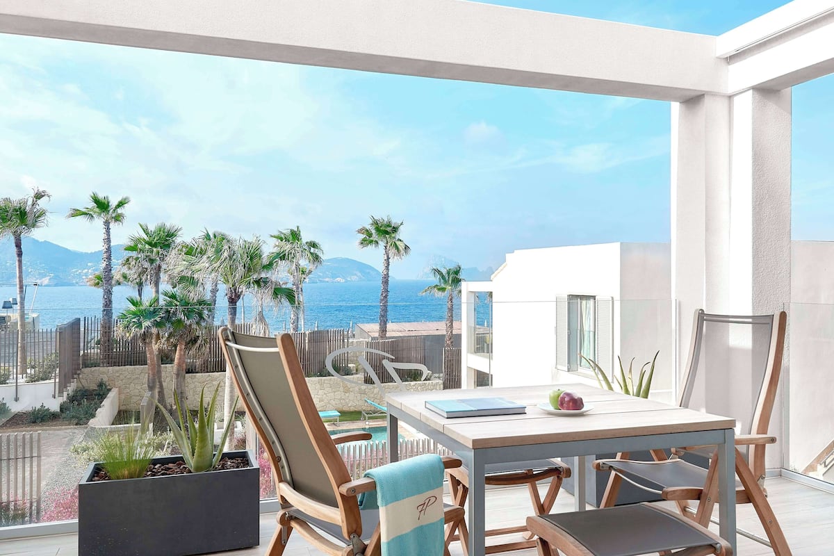 Un balcón con vista al mar, palmeras y una piscina.