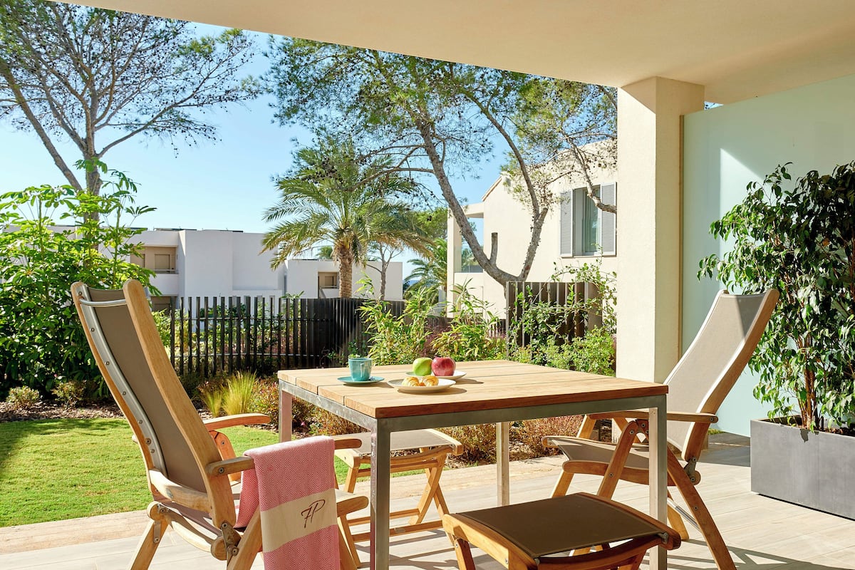 Un patio al aire libre con una mesa y sillas de madera, un pequeño jardín y vistas a una zona residencial.