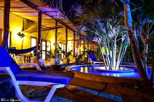 Un área de piscina con sillas de descanso, una piscina pequeña y plantas tropicales.