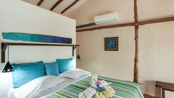 Een hotelkamer met een bed, hoofdbord, een wandgemonteerde airconditioner, een ingelijste foto en een houten bankje.