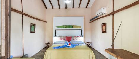 A hotel room with a bed, a wooden bench, a hanging hammock, and a ceiling fan.