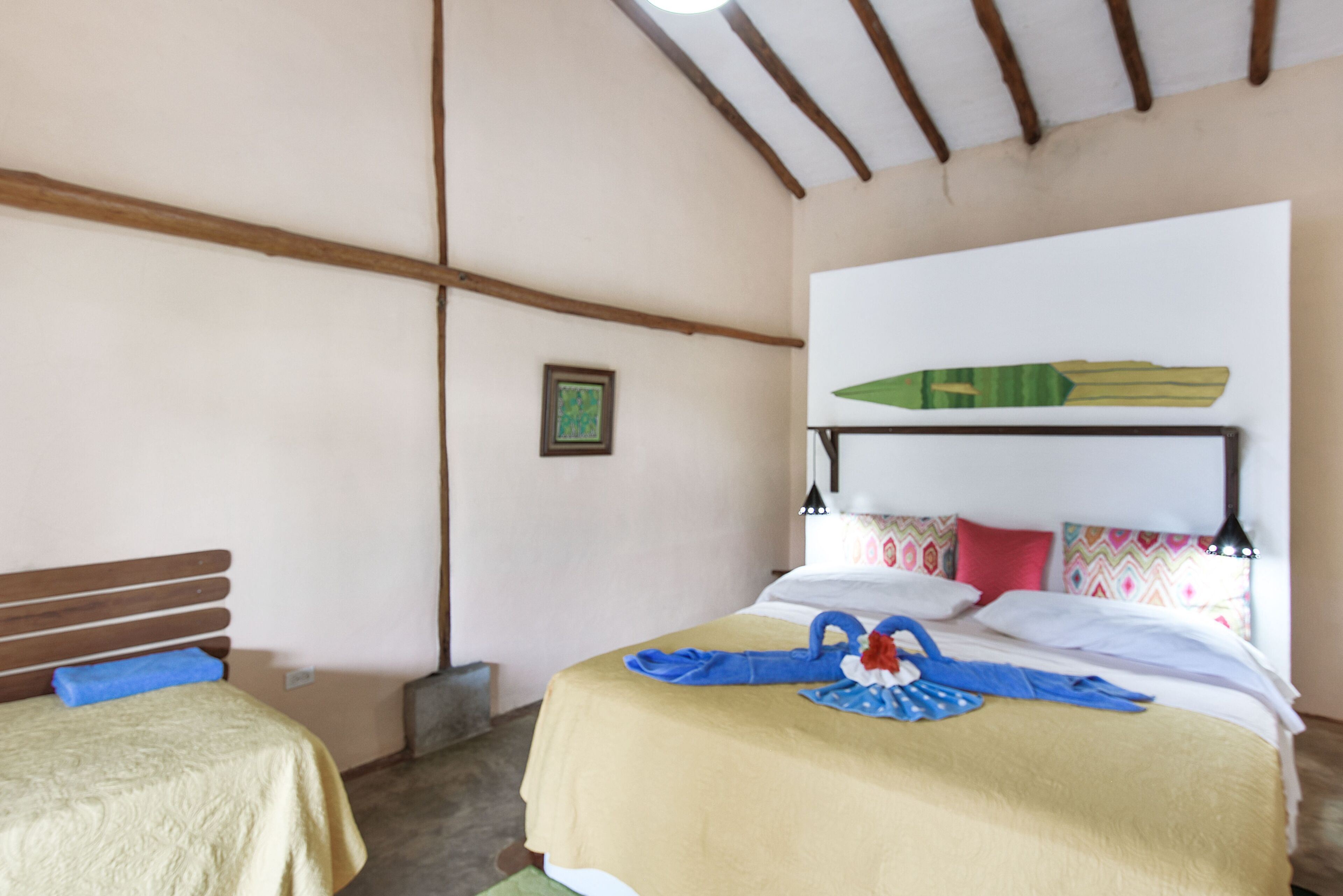 Una habitación con una cama, una cama más pequeña, vigas de madera en el techo y un cuadro en la pared.