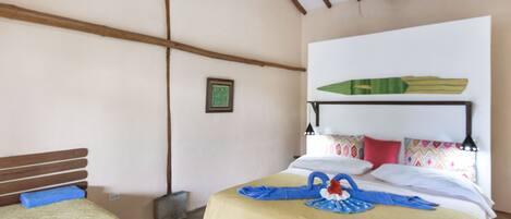 Una habitación con una cama, una cama más pequeña, vigas de madera en el techo y un cuadro en la pared.
