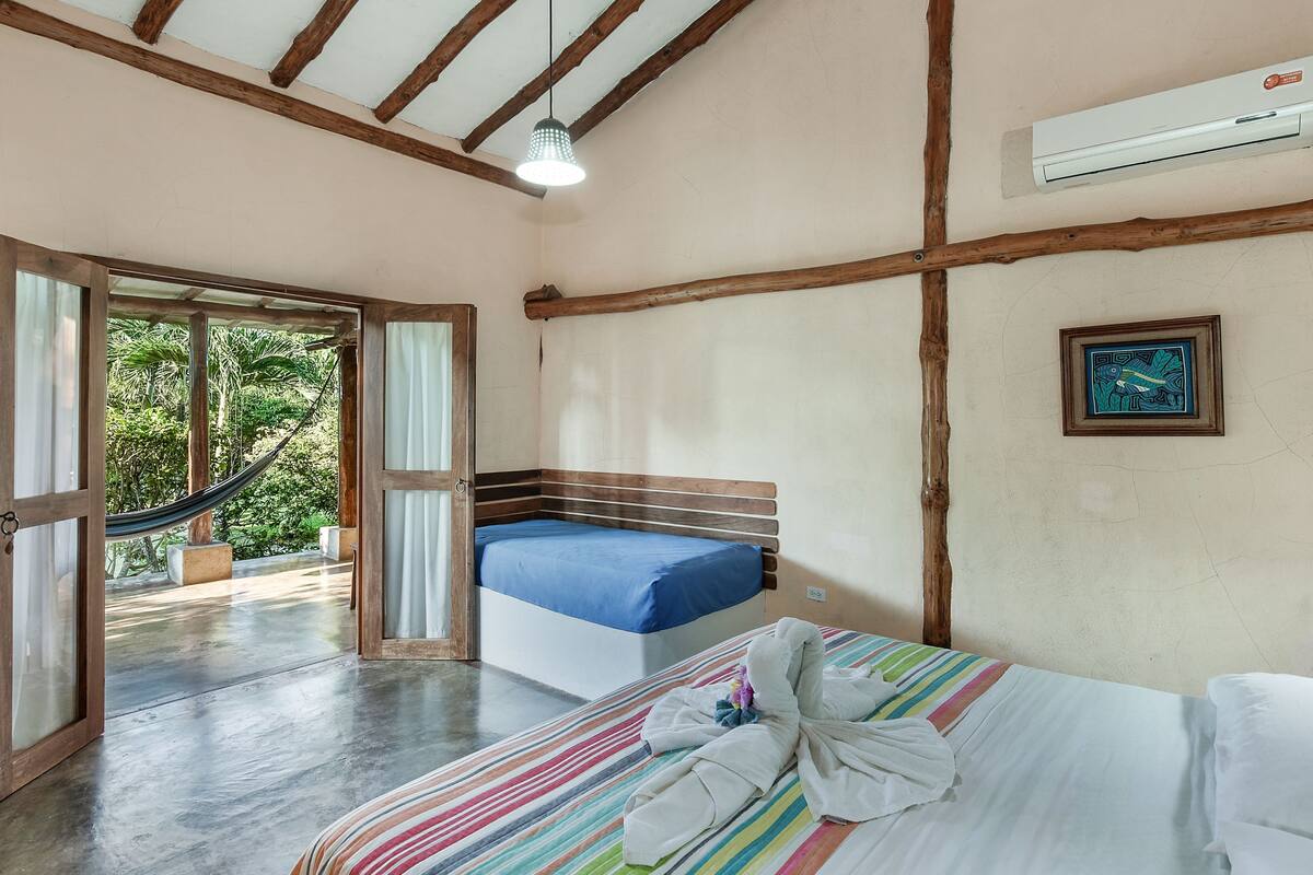 A bedroom with a bed, a hammock, and a view of greenery outside.