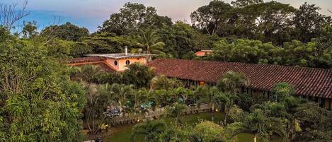 A large building with a red-tiled roof surrounded by lush greenery and trees.