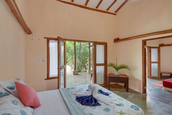A bedroom with a bed, a bedside table, a potted plant, and a view of the outside. - Casa Lajagua (Pedasí)