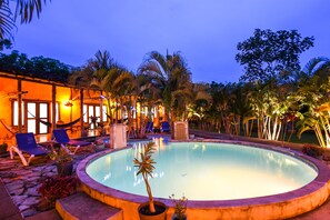 Una piscina circular rodeada de sillones de descanso y palmeras, con un edificio al fondo.