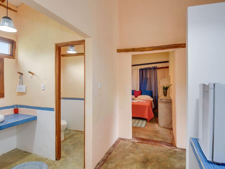 A bathroom with a sink, mirror, and towel rack. There is a door leading to a bedroom with a bed and curtains.
