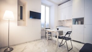 A modern kitchen with white cabinets, a dining table with two chairs, a floor lamp, and a TV on the wall. - The golden keys rome (Rome)