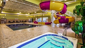 Una piscina interior con jacuzzi, tobogán de agua y zona de estar con sillas y mesas.