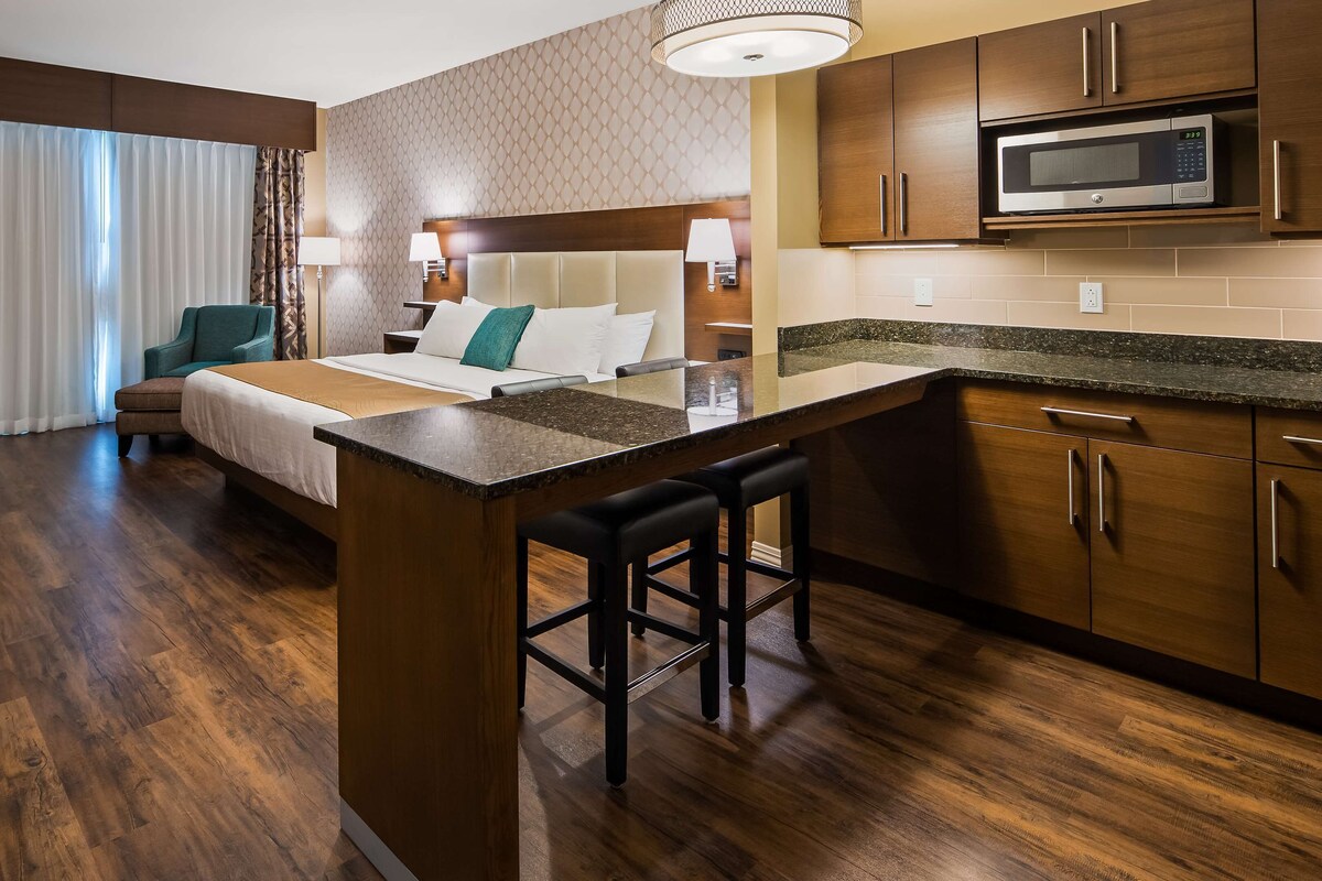 A hotel room with a bed, a desk, a chair, a kitchenette, and a bathroom.