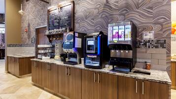 A coffee station with multiple machines, a chalkboard menu, and a waste bin.