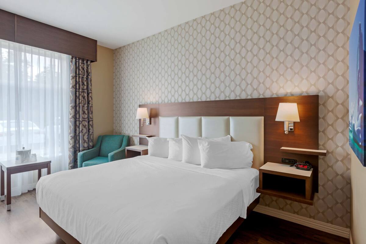 A hotel room with a large bed, a nightstand with a lamp, a chair, and a small table.