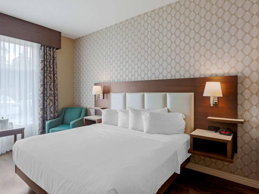 Ein Hotelzimmer mit einem großen Bett, einem Nachttisch mit Lampe, einem Sessel und einem kleinen Tisch.