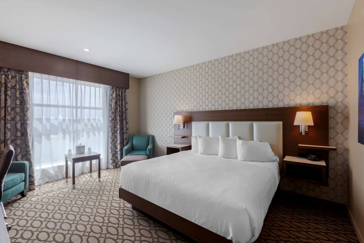 A hotel room with a large bed, a nightstand, a chair, a table, and a window with curtains.