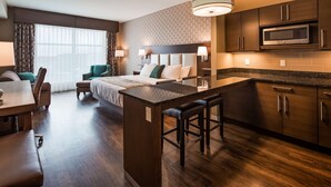 Una habitación de hotel moderna con kitchenette, comedor y una cama grande con cabecera.