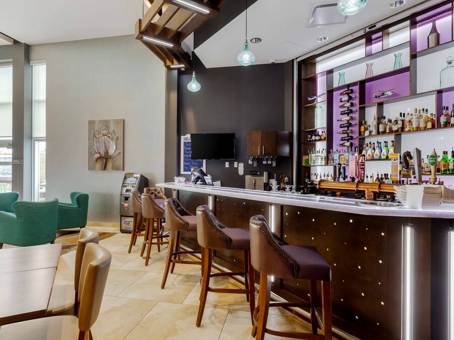 A bar area with a long counter, bar stools, and a variety of bottles.