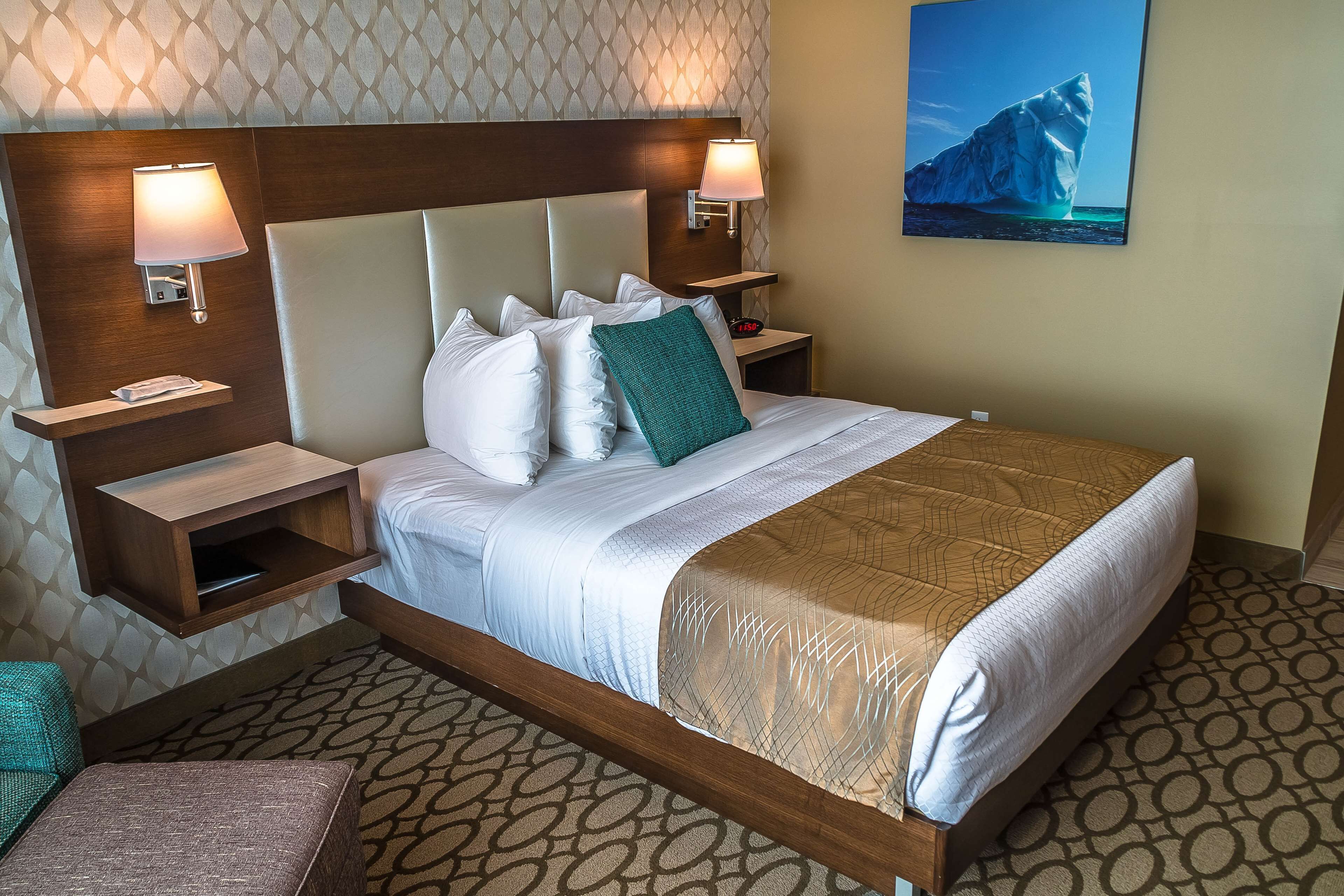 A hotel room with a large bed, two bedside tables, a nightstand, a wall-mounted clock, and a painting of an iceberg.