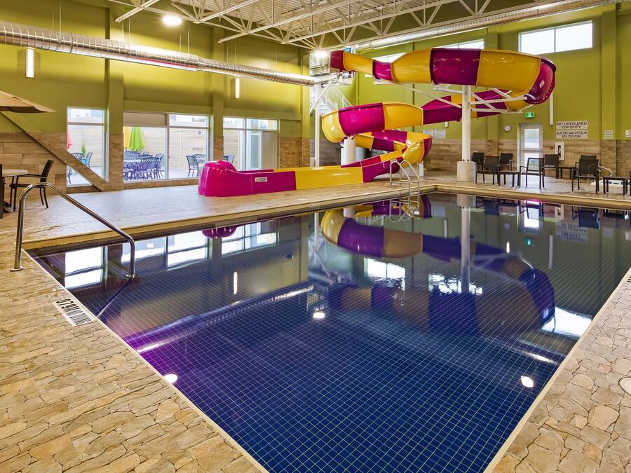 An indoor swimming pool with a water slide, stone flooring, and a seating area with tables and chairs.