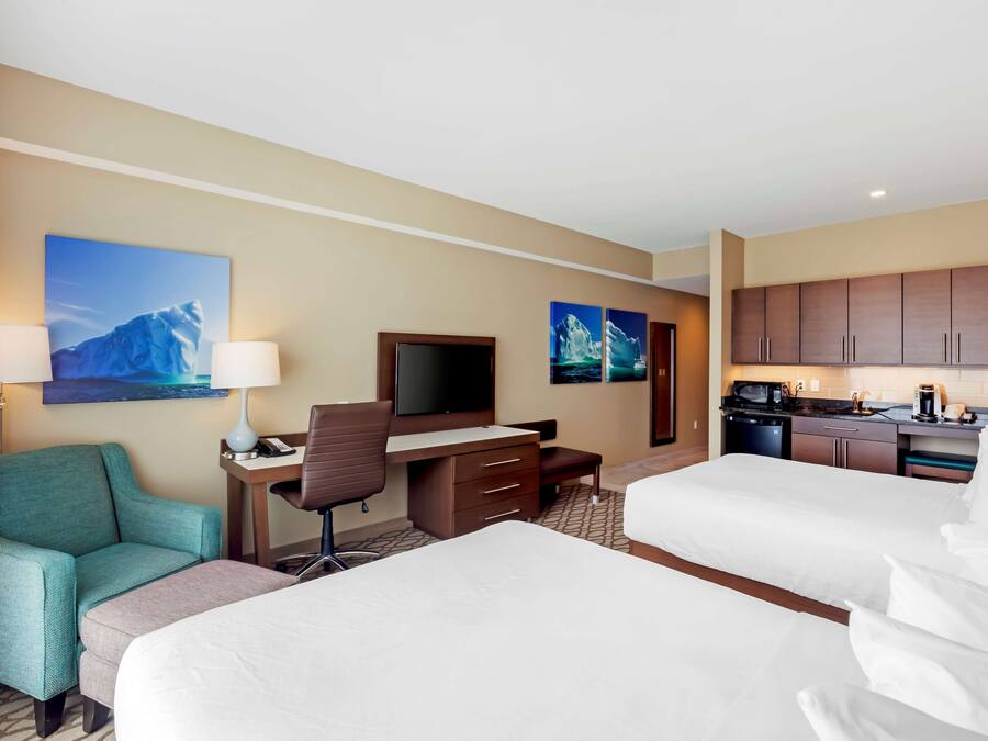 A hotel room with two beds, a desk with a chair, a television, and a kitchenette.