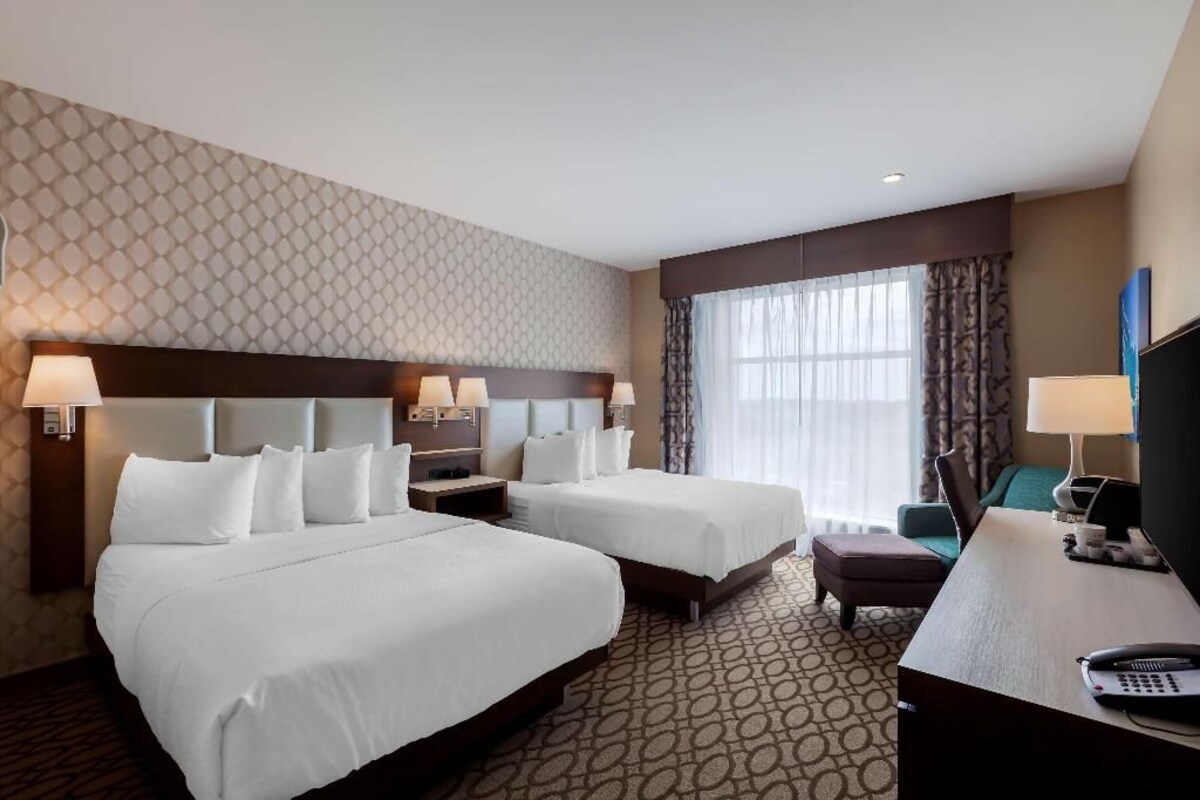 A hotel room with two beds, a desk, a chair, a TV, and a window with curtains.