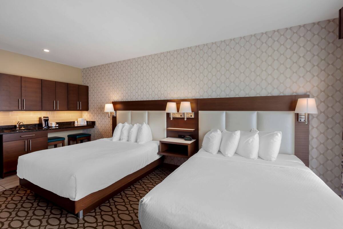 A hotel room with two beds, a kitchenette, and a patterned wallpaper.
