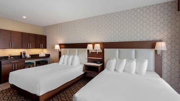A hotel room with two beds, a kitchenette, and a patterned wallpaper.
