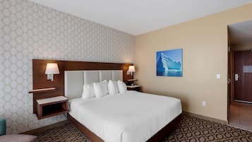 A hotel room with a large bed, a headboard with built-in lighting, a nightstand, a wall-mounted shelf, and a painting of a mountain landscape.