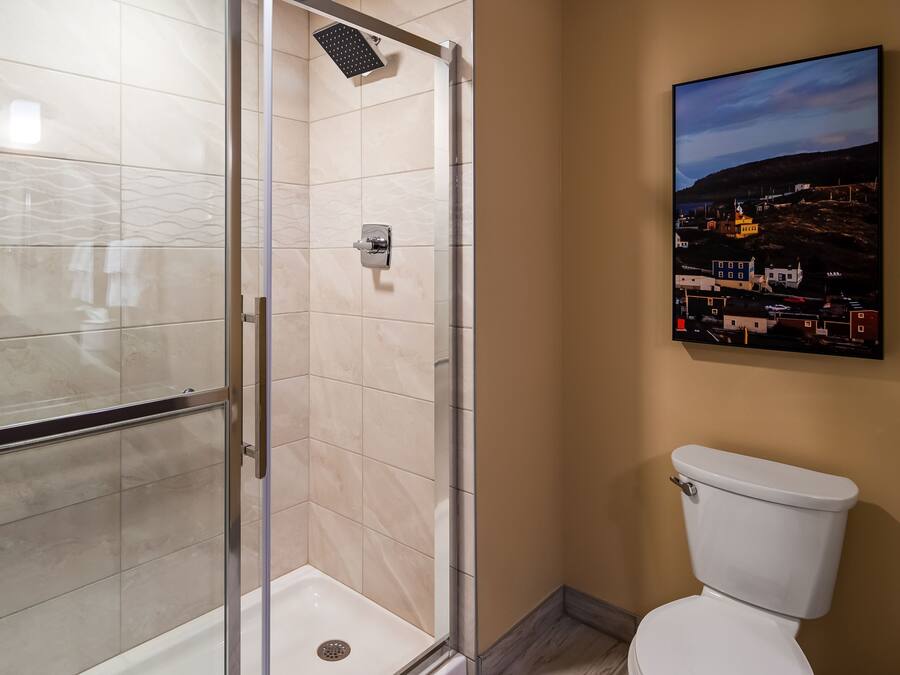 A bathroom with a glass-enclosed shower, a toilet, and a painting on the wall.