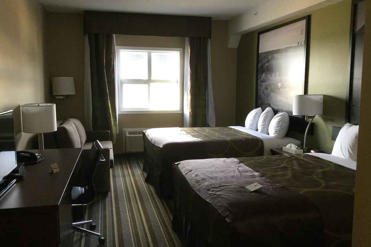 Habitación de hotel con dos camas, un escritorio, una silla, un televisor y una ventana con cortinas.