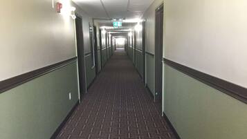 A hotel hallway with carpeted floors, doors on both sides, and a lighted exit sign at the end.