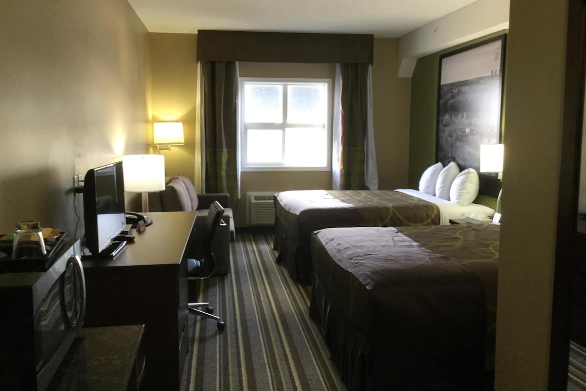 Una habitación de hotel con dos camas, un escritorio con ordenador, una silla y una ventana con cortinas.