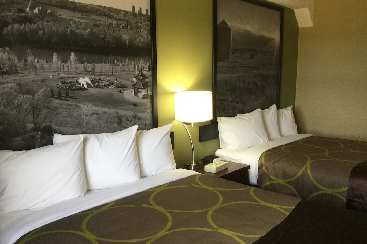 Una habitación de hotel con una cama grande, una mesita de noche, una lámpara y un cuadro colgado en la pared.