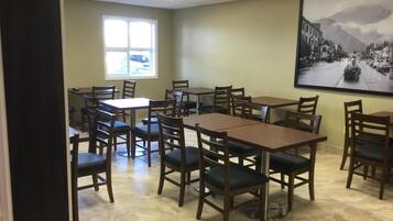 Une salle de conférence avec plusieurs tables et chaises, une grande fenêtre donnant sur une voiture et un tableau encadré accroché au mur.