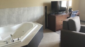 A modern bathroom with a large bathtub, a vanity with a mirror, and a flat-screen TV on a wooden dresser. - Super 8 by Wyndham Hardisty (Hardisty)