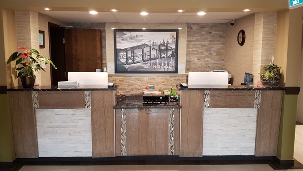 A reception desk with a framed welcome sign, a clock, and potted plants. - Super 8 by Wyndham Hardisty (Hardisty)