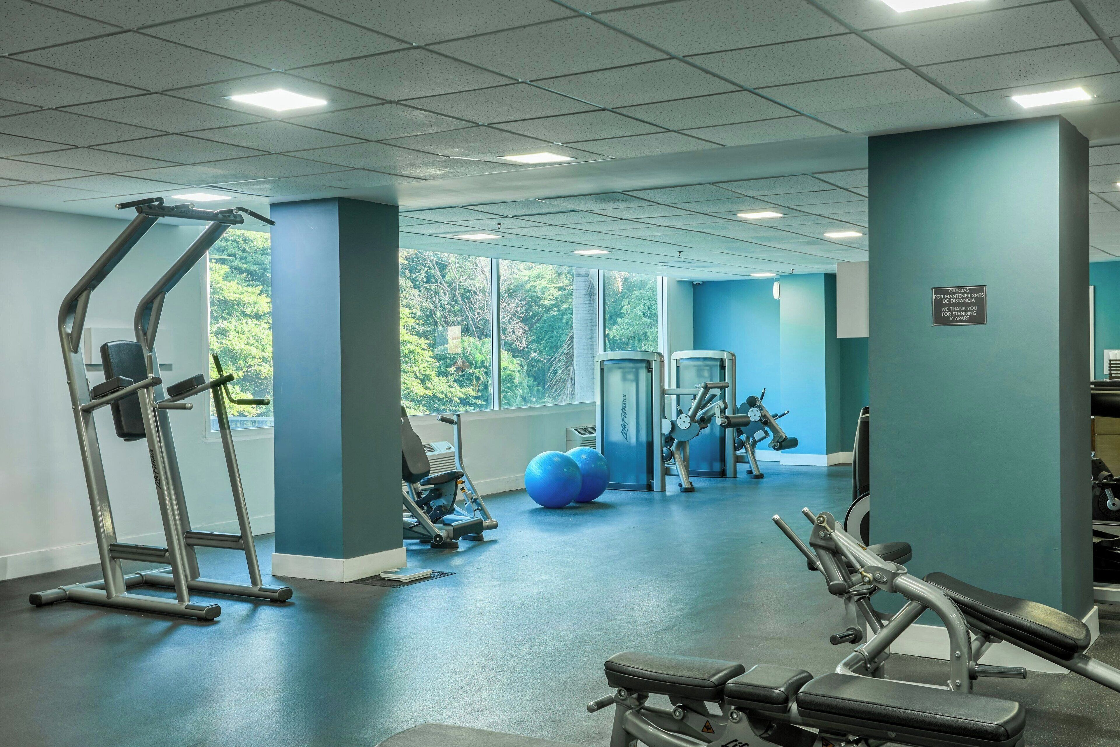 Ein Fitnessraum mit Trainingsgeräten, großen Fenstern und Blick auf Grünflächen.