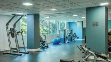 Ein Fitnessraum mit Trainingsgeräten, großen Fenstern und Blick auf Grünflächen.