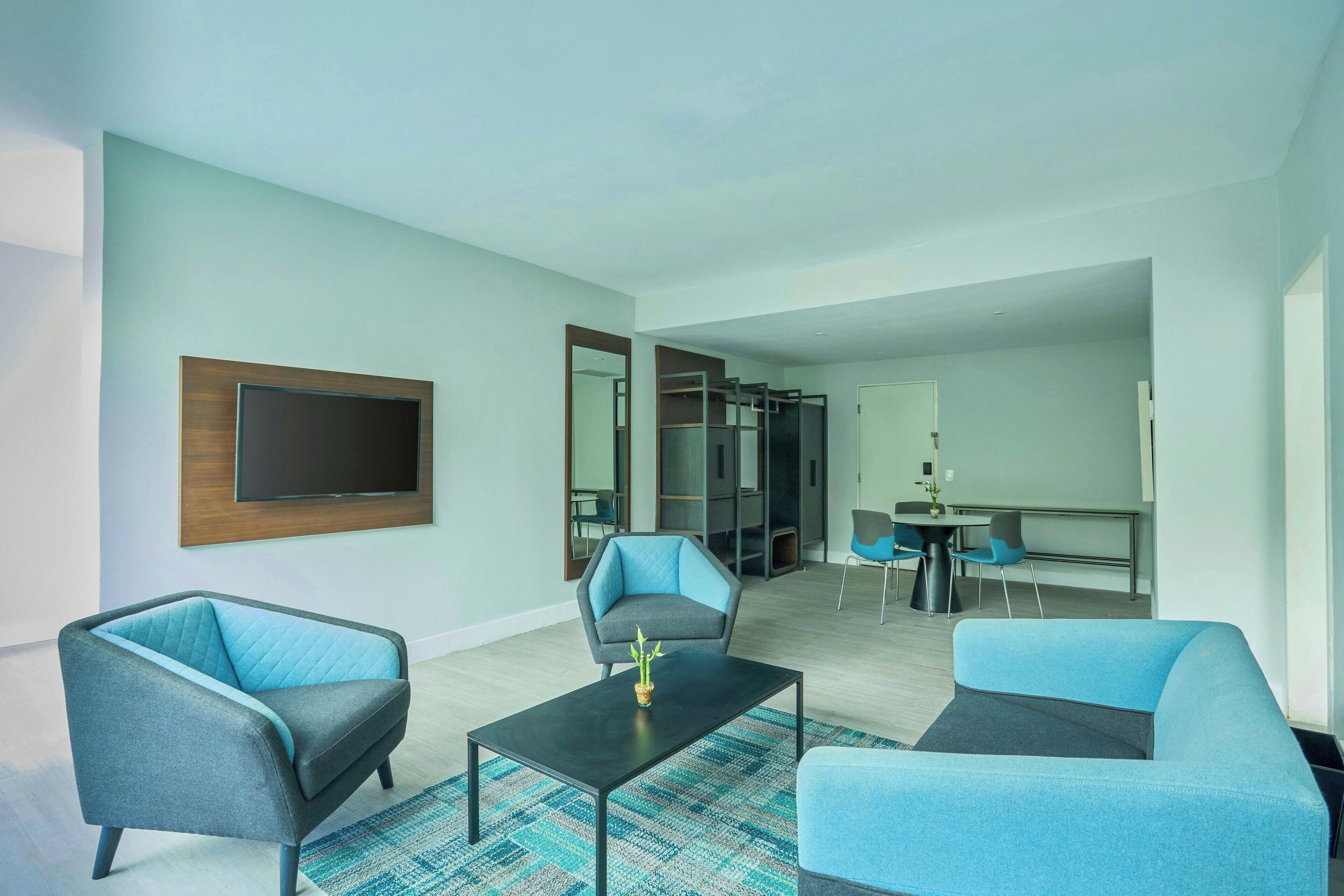 Een moderne woonkamer met een flatscreen televisie, twee banken, een salontafel en een eethoek met een kleine tafel en stoelen.